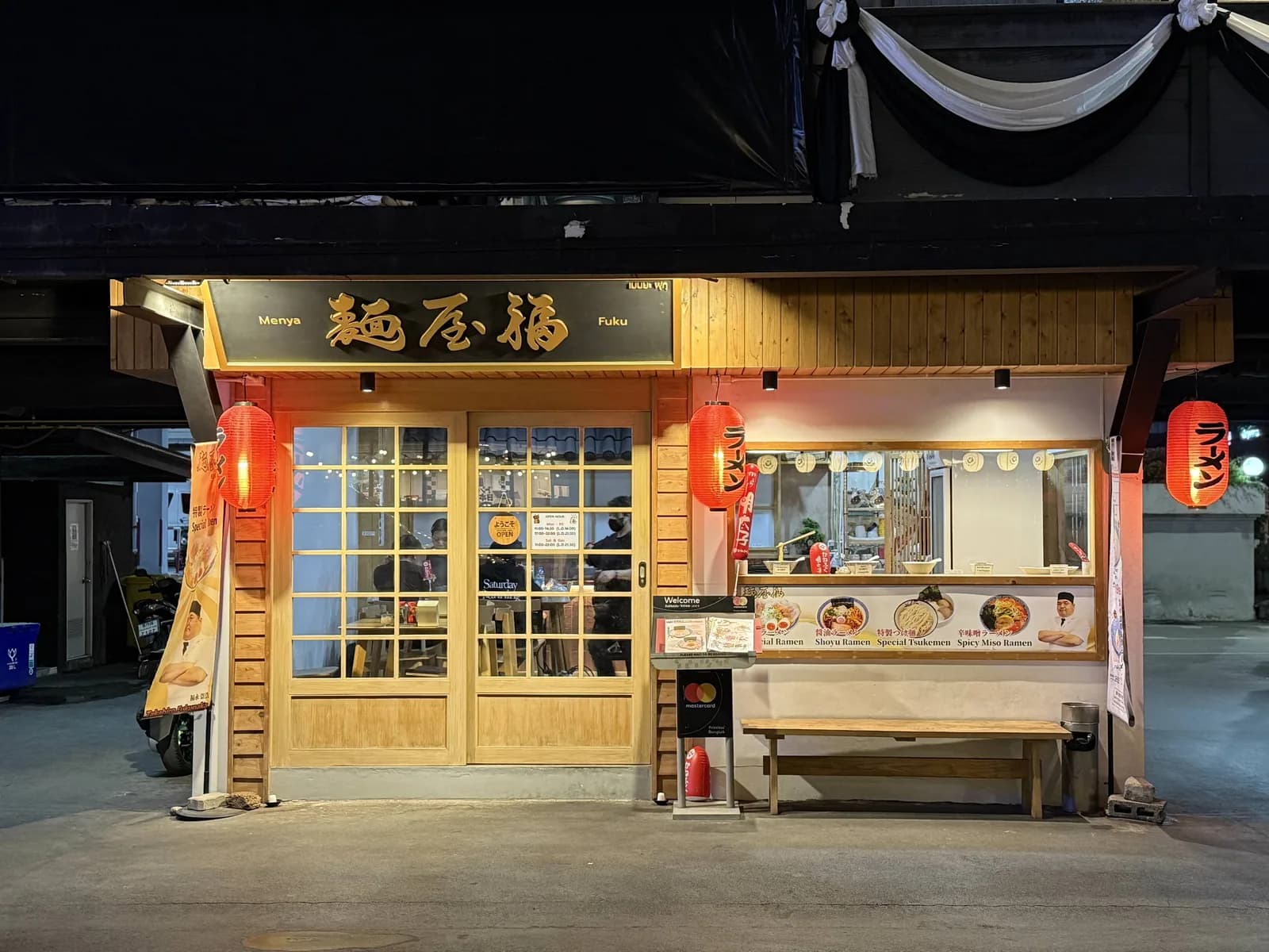 夜の麺屋 福の外観。金色の「麺屋 福」の看板と赤いラーメン提灯が灯り、木の引き戸に「ようこそ OPEN」の札が出ている